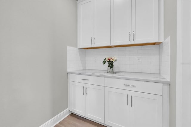 bar featuring light wood-style flooring, baseboards, and decorative backsplash