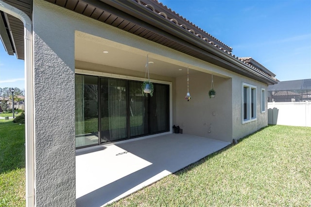 rear view of property featuring a patio, fence, a tile roof, a lawn, and stucco siding