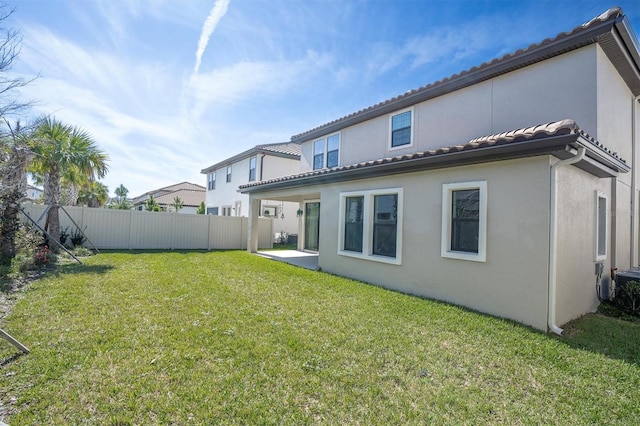 rear view of property featuring a tile roof, a patio, stucco siding, a lawn, and fence