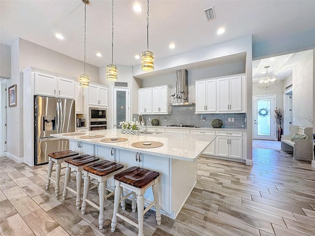 kitchen with visible vents, backsplash, appliances with stainless steel finishes, white cabinetry, and wall chimney range hood