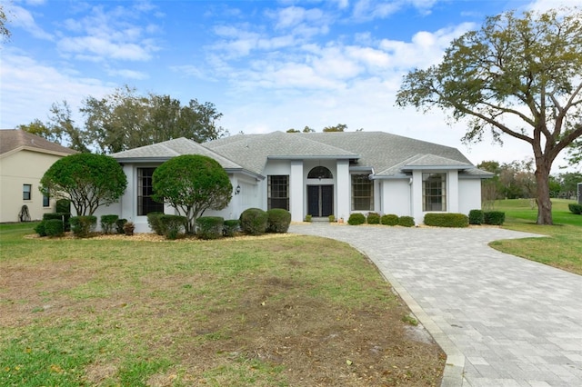 view of front of house featuring a shingled roof, decorative driveway, a front yard, and stucco siding