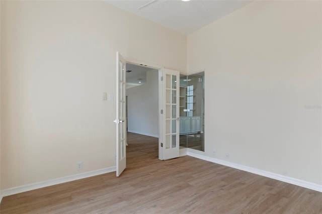 empty room with baseboards, french doors, and light wood-style floors