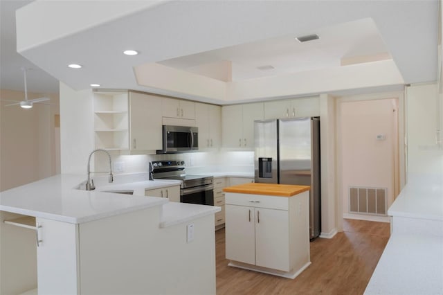 kitchen with open shelves, visible vents, appliances with stainless steel finishes, a sink, and a peninsula