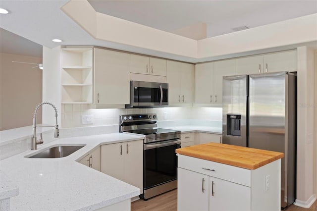 kitchen with butcher block counters, a sink, appliances with stainless steel finishes, backsplash, and open shelves