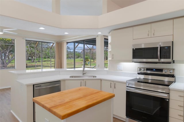 kitchen featuring a peninsula, a sink, stainless steel appliances, wooden counters, and backsplash