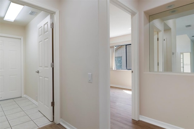 hall with light tile patterned flooring, visible vents, and baseboards