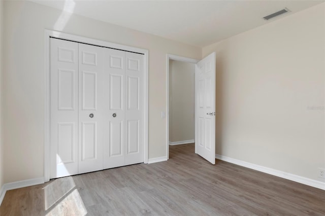 unfurnished bedroom featuring baseboards, a closet, visible vents, and wood finished floors