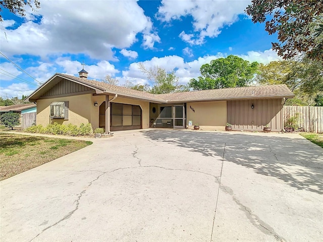 ranch-style home with a garage, concrete driveway, fence, and stucco siding