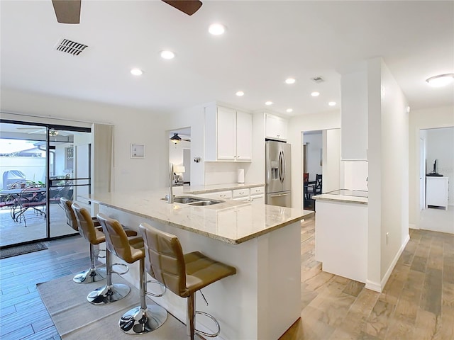 kitchen with light wood-style flooring, a sink, white cabinetry, light stone countertops, and stainless steel fridge