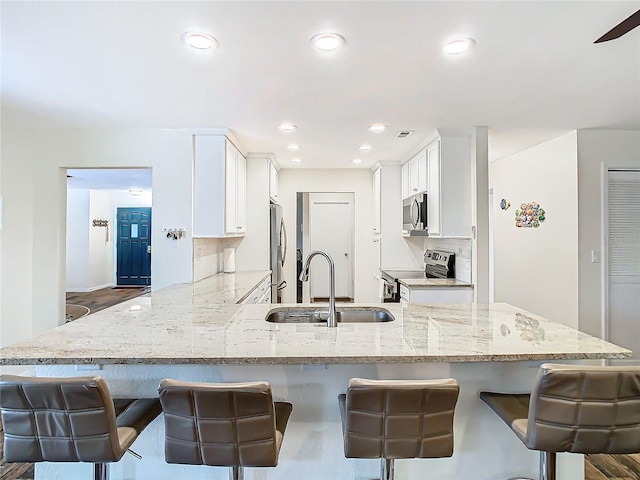 kitchen featuring appliances with stainless steel finishes, a sink, light stone countertops, and white cabinets