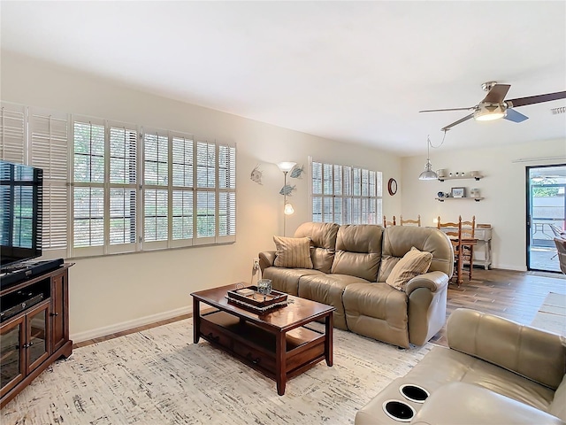 living area with light wood-type flooring, visible vents, baseboards, and a ceiling fan