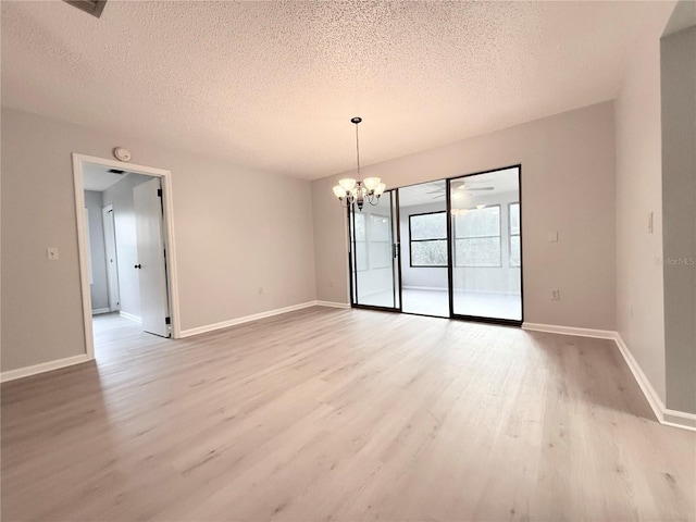 unfurnished room featuring light wood-style floors, a textured ceiling, baseboards, and an inviting chandelier