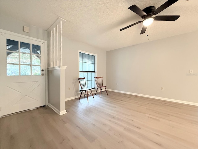 interior space with a ceiling fan, baseboards, light wood-style flooring, and a textured ceiling