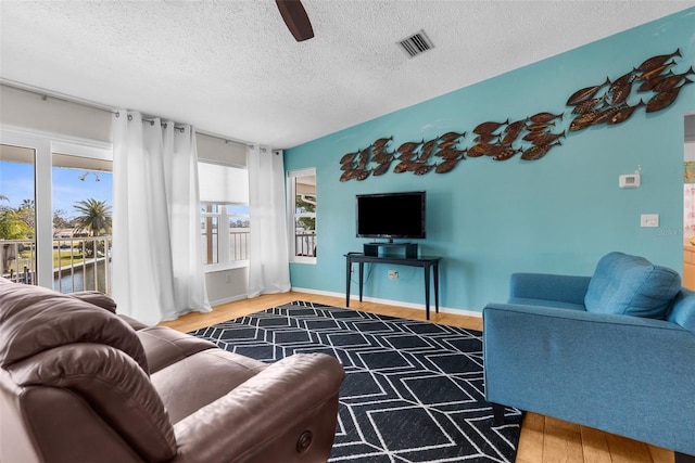 living room featuring a textured ceiling, ceiling fan, wood finished floors, visible vents, and baseboards