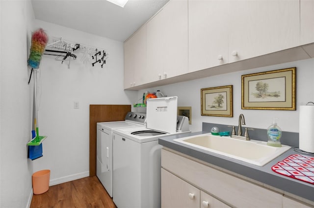 washroom featuring cabinet space, washing machine and dryer, a sink, wood finished floors, and baseboards