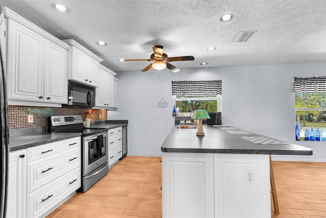 kitchen featuring black microwave, a kitchen island, visible vents, electric stove, and dark countertops