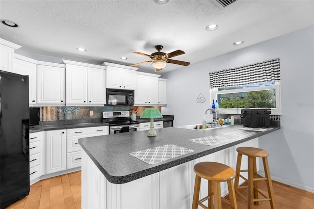 kitchen featuring dark countertops, a breakfast bar area, a sink, black appliances, and backsplash