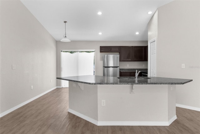 kitchen featuring wood finished floors, a sink, freestanding refrigerator, and dark brown cabinetry