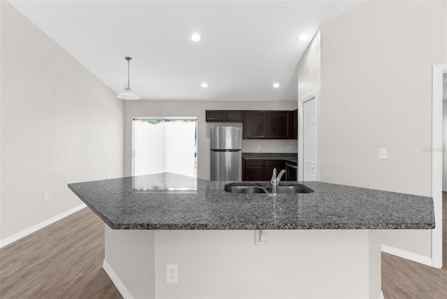 kitchen with dark brown cabinetry, a sink, light wood-type flooring, freestanding refrigerator, and an island with sink