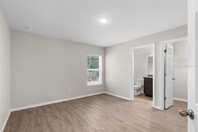unfurnished bedroom with ensuite bathroom, baseboards, light wood-style floors, a spacious closet, and a closet
