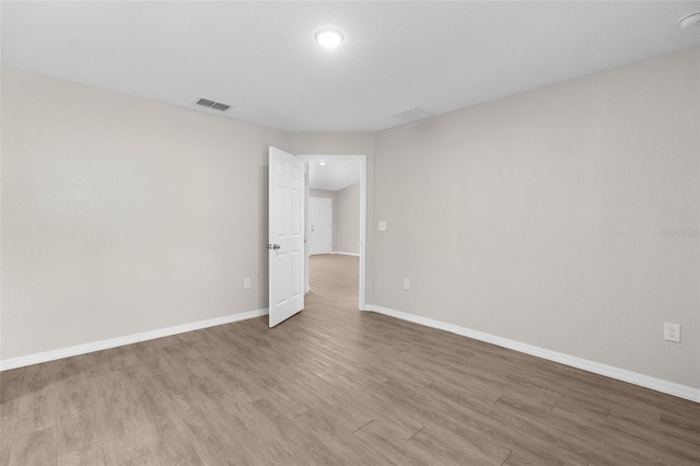 empty room featuring wood finished floors, visible vents, and baseboards