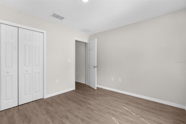 unfurnished bedroom with visible vents, a closet, baseboards, and wood finished floors