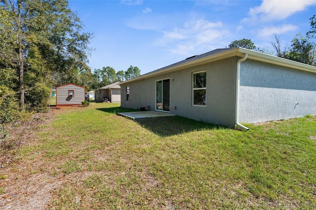 back of property with an outbuilding, a patio, a yard, stucco siding, and a shed