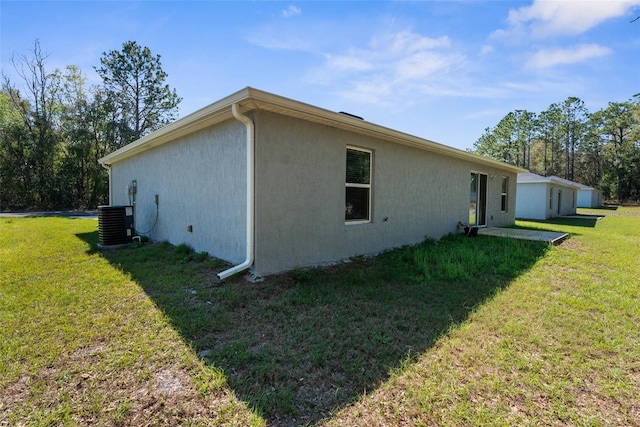 view of side of home featuring stucco siding, a yard, and central air condition unit