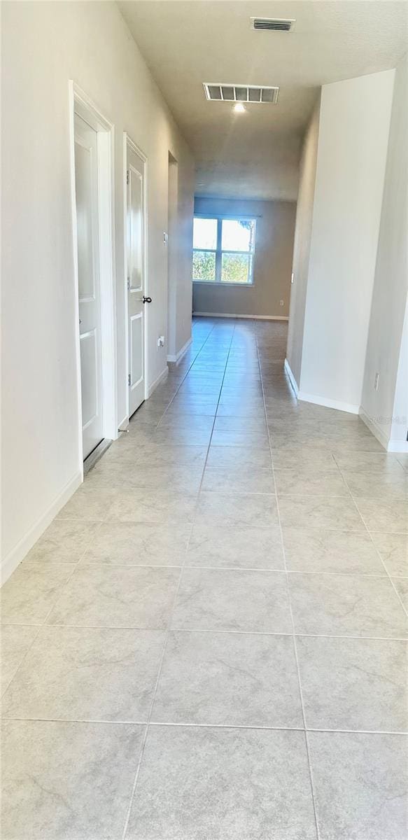 corridor featuring light tile patterned flooring, visible vents, and baseboards