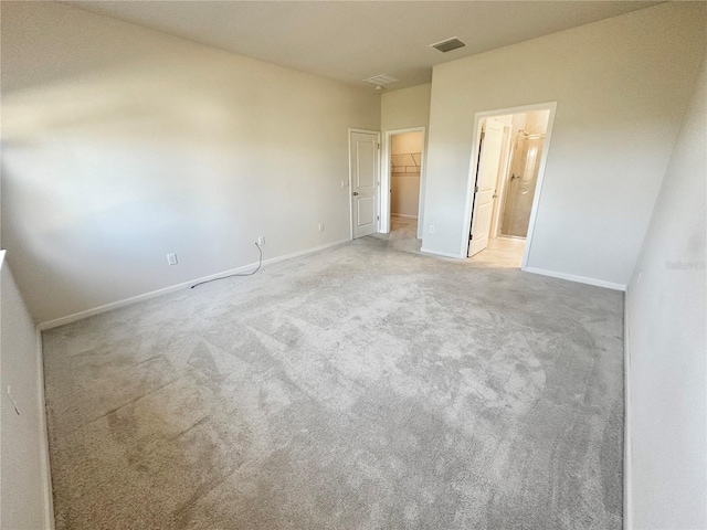 unfurnished bedroom featuring visible vents, a spacious closet, carpet flooring, ensuite bath, and baseboards