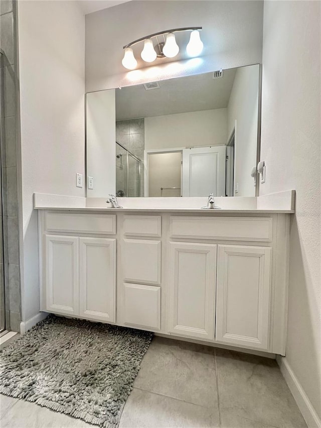 bathroom with double vanity, a stall shower, visible vents, and baseboards