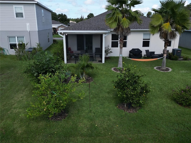 back of house with a sunroom, roof with shingles, stucco siding, and a yard