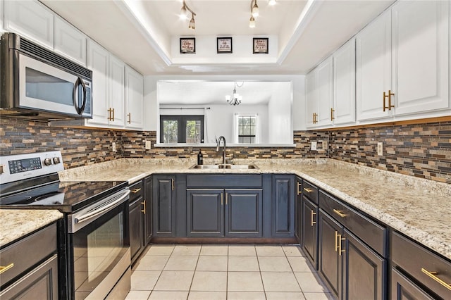 kitchen with light tile patterned floors, a raised ceiling, appliances with stainless steel finishes, white cabinetry, and a sink