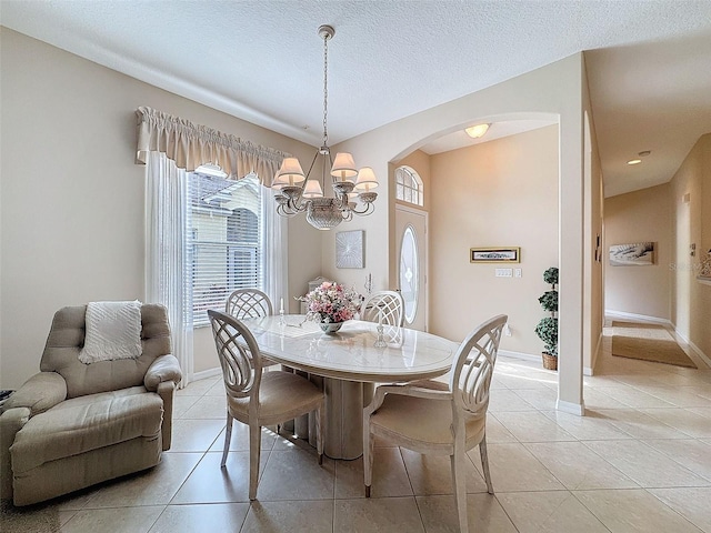 dining space featuring light tile patterned floors, baseboards, arched walkways, and a textured ceiling