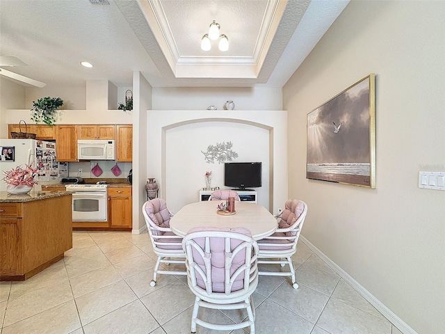 dining space with light tile patterned floors, a textured ceiling, baseboards, a raised ceiling, and crown molding