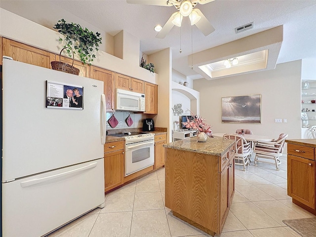 kitchen featuring white appliances, visible vents, brown cabinets, a center island, and light tile patterned flooring