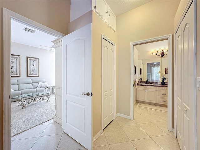 hall featuring light tile patterned floors, a textured ceiling, a sink, and visible vents