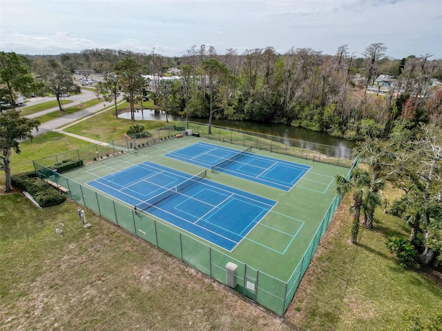 view of tennis court featuring a water view, fence, and a lawn