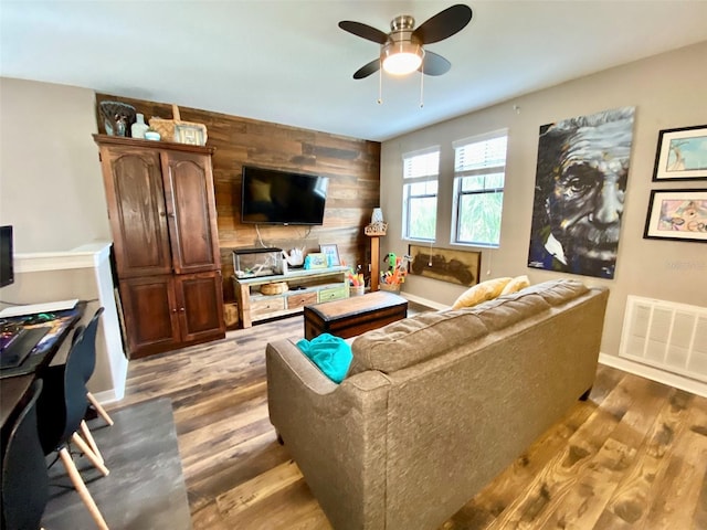 living area with wooden walls, baseboards, visible vents, an accent wall, and wood finished floors