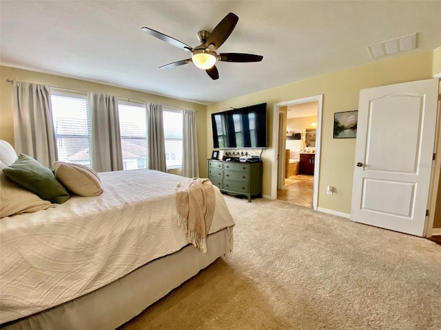 bedroom featuring ceiling fan, light carpet, visible vents, baseboards, and ensuite bath