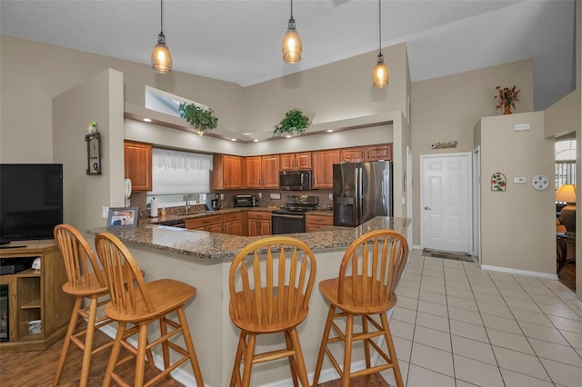 kitchen with brown cabinetry, a peninsula, stainless steel appliances, a kitchen bar, and a sink