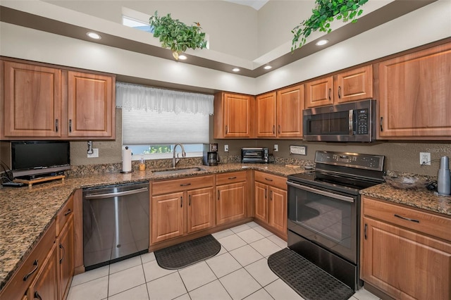 kitchen featuring stainless steel appliances, dark stone counters, brown cabinets, and a sink