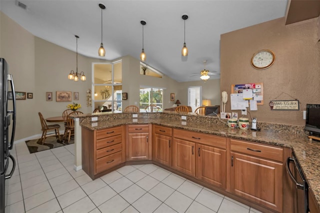 kitchen with brown cabinetry, hanging light fixtures, dark stone countertops, and ceiling fan with notable chandelier