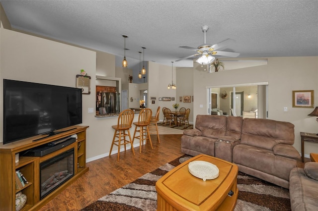 living room with a ceiling fan, a glass covered fireplace, wood finished floors, vaulted ceiling, and a textured ceiling