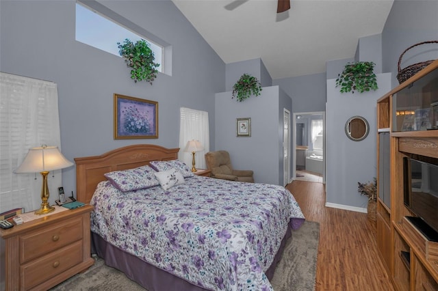 bedroom with a glass covered fireplace, ceiling fan, connected bathroom, high vaulted ceiling, and light wood-type flooring