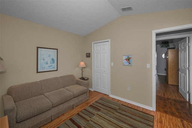 living room with visible vents, vaulted ceiling, a textured ceiling, wood finished floors, and baseboards