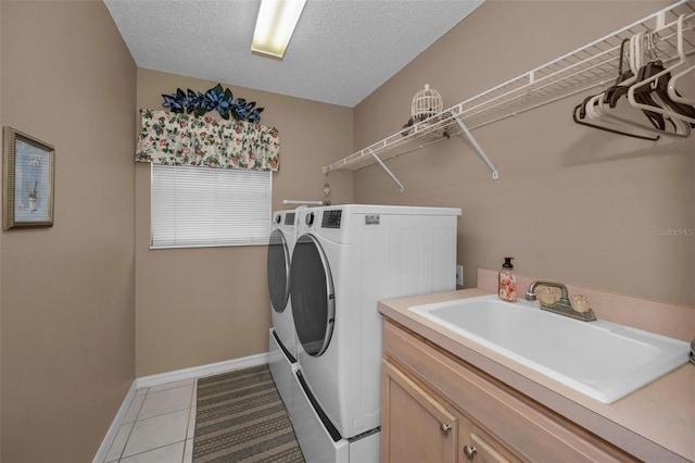 washroom featuring a textured ceiling, a sink, cabinet space, tile patterned floors, and washing machine and clothes dryer