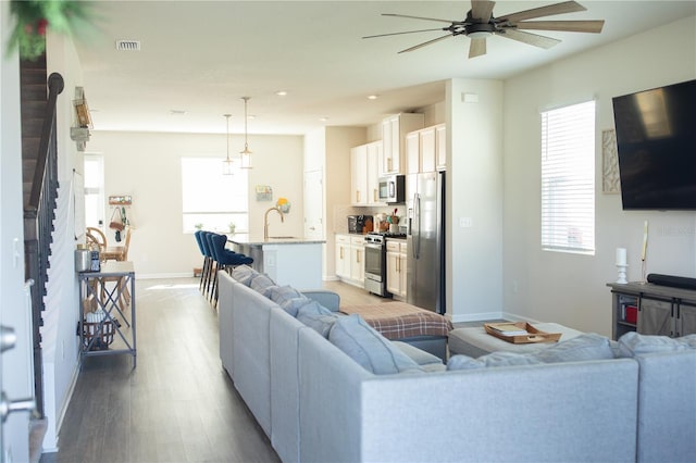 living area featuring ceiling fan, wood finished floors, visible vents, baseboards, and stairway