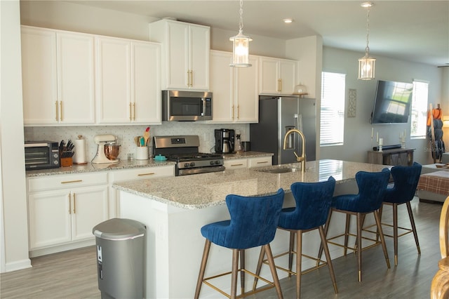 kitchen featuring a center island with sink, light wood-style flooring, decorative backsplash, appliances with stainless steel finishes, and white cabinets