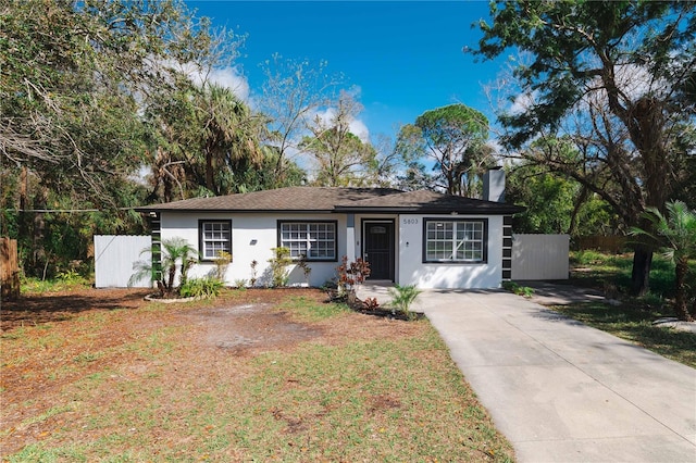 ranch-style home with driveway, fence, a chimney, and stucco siding